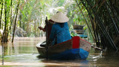 Vietnam woman in conical hat sailing at boat through mekong delta jungle canal, Vietnam