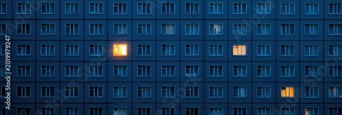 A warm light glows from one apartment window in a large dark building, standing out against the cold exterior in the night.