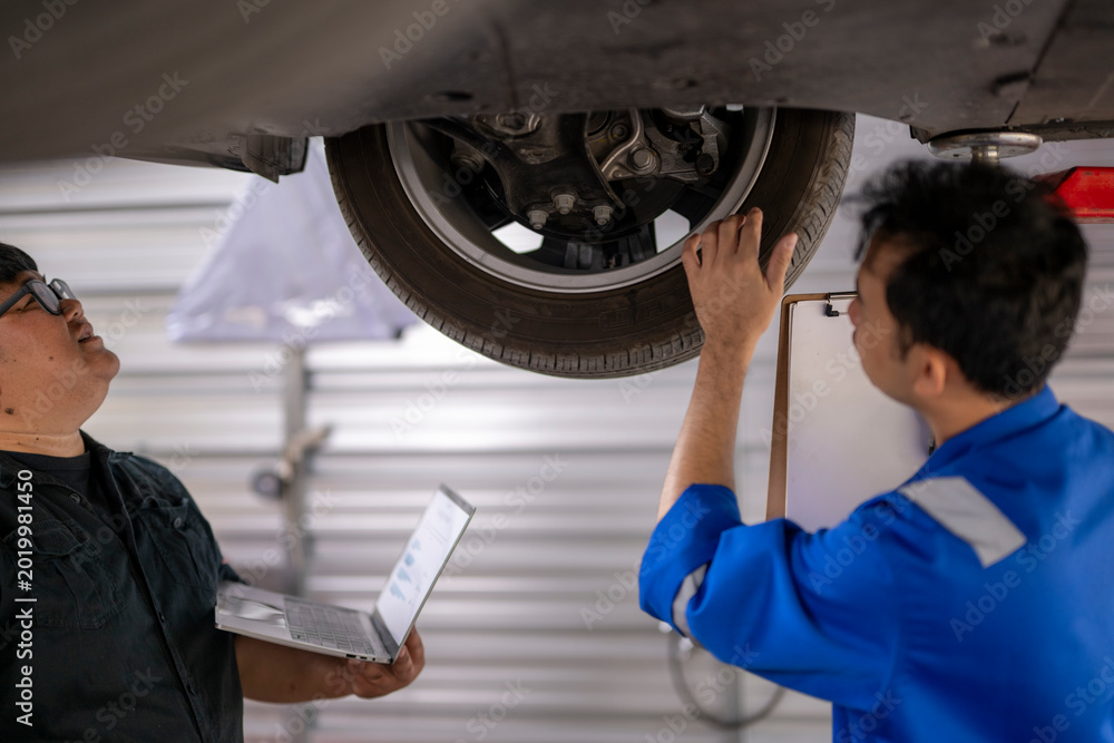 Obraz premium Auto mechanics team inspecting car undercarriage with laptop