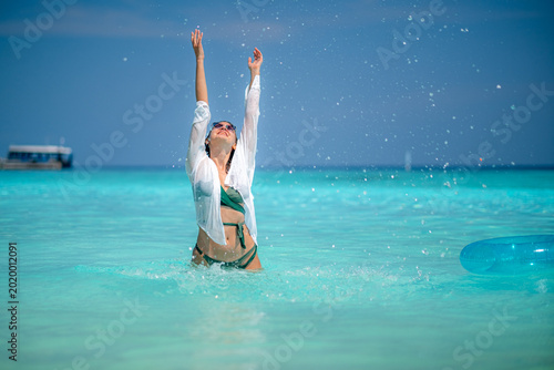 Tableau sur toile A woman, wearing a swimsuit, enjoys a vacation on a sandy beach with turquoise water, holding a blue floatation device, a tranquil holiday setting