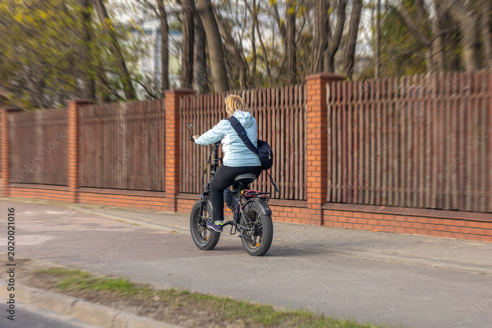 Naklejka premium Woman riding electric bicycle on bike path. Active person travels through city on bike.