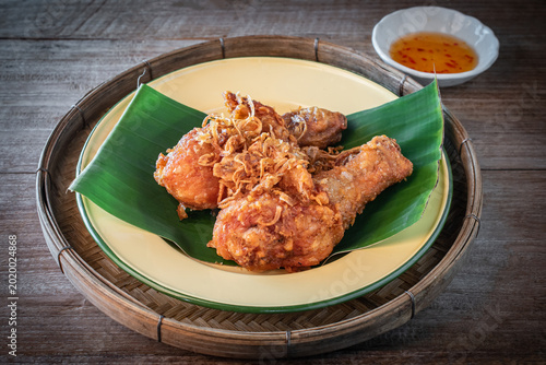Canvastavla Authentic Hat Yai fried chicken drumsticks topped with crispy fried shallots served on a green banana leaf in a wooden tray