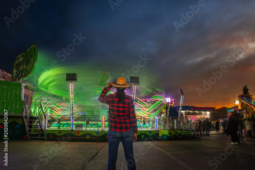 Woman watching carnival ride at sunset with motion blur lights
