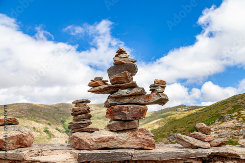 Stacked balanced stones creating cairns on a mountain wall under a blue sky, symbolizing harmony and peace