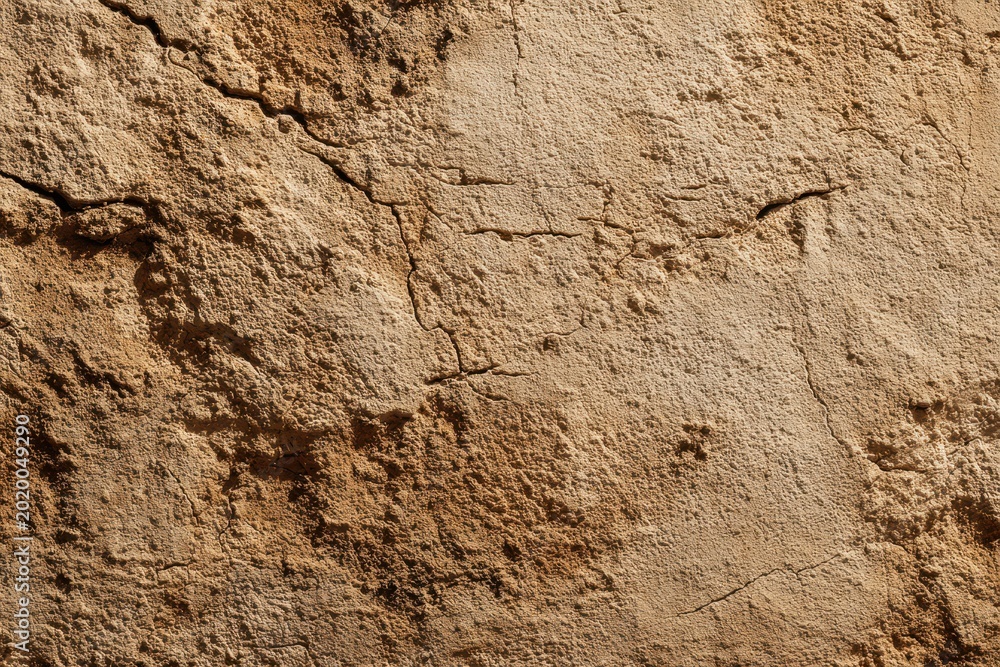 Fototapeta premium Close-up of rough mud wall texture with cracks and earthy tones