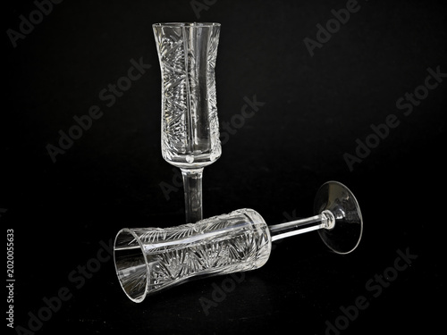 Two vintage cut crystal champagne flutes on a black background, elegant glassware with ornate etched patterns and reflective details.
