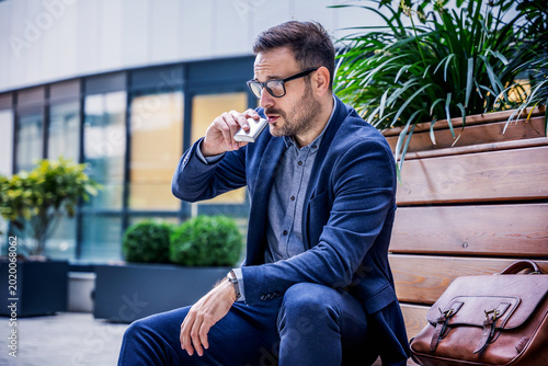 Stressed businessman drinking alcohol during work break near modern office building