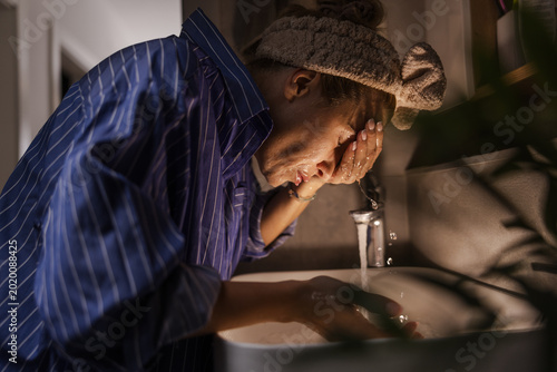 Person Washing Face in Bathroom Sink During Nighttime Routine After Long Day at Home