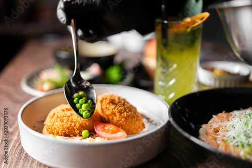 Foto A chef in black gloves places green peas from a spoon onto crispy fried croquett