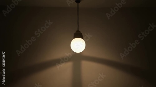 Dimming Light Bulb Hanging from Ceiling in Dark Room