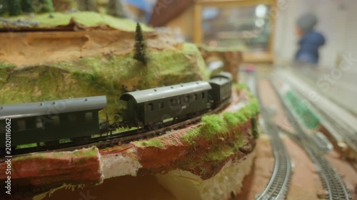 A fixed-shot scene showing a green freight train emerging from a cave on the right and speeding past before exiting on the left in a miniature landscape world