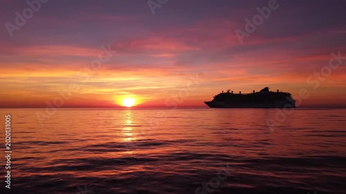 Cruise ship sailing into vibrant sunset.