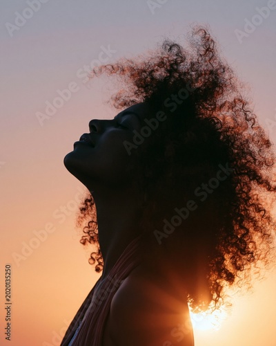 Silhouette portrait of woman with curly hair at sunset