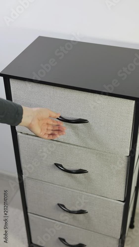 Vertical video of woman putting a folded blue towel into a modern fabric storage dresser drawer. Close up, footage.
