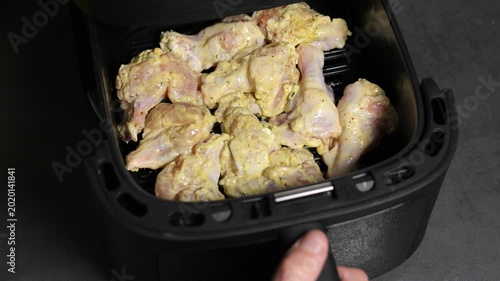 Hand closing marinated raw chicken pieces inside air fryer for to start cooking.