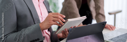 business women writing notes in notebook during office meeting discussion corporate team collaboration planning strategy brainstorming ideas at workplace