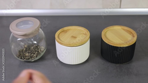 Hand opening a white ceramic jar filled with high-quality loose leaf green tea leaves.