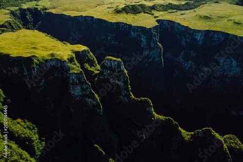Quadro em tela Dramatic drone view of deep canyon cliffs with green plateau and rugged landscap