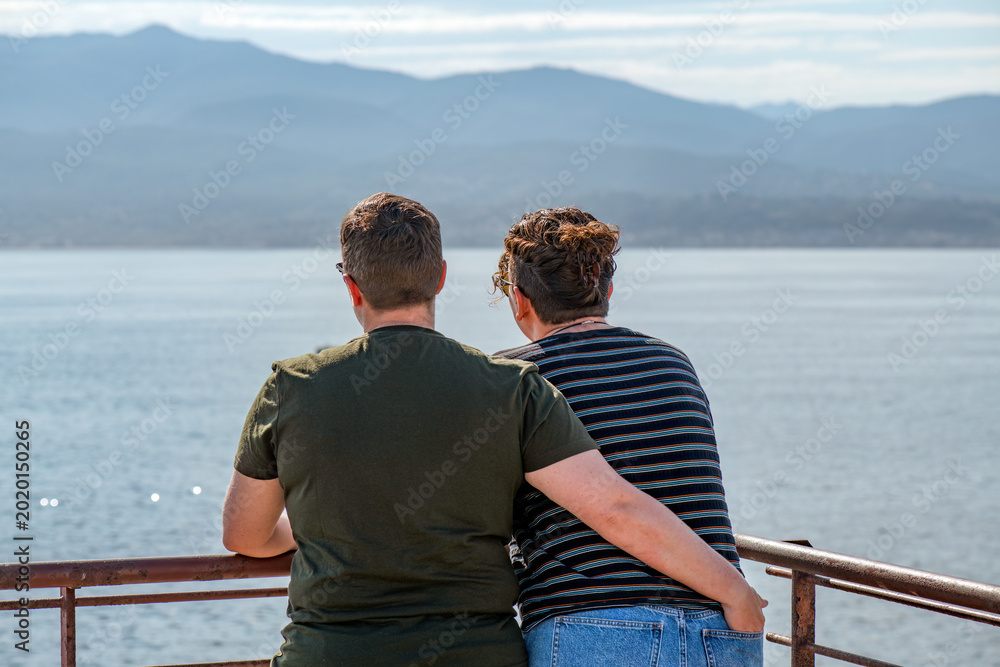 Fototapeta premium A woman in her thirties has her hand in her wife's back pocket as they look over the sea and mountains on Corsica.