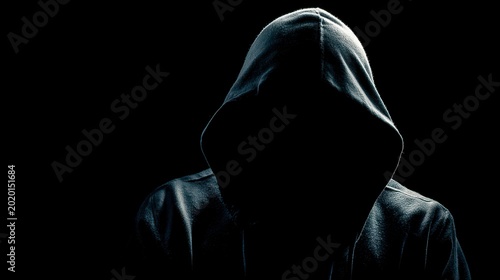 A person in a hooded sweatshirt, their face obscured in shadow. The image is a stark contrast of light and dark