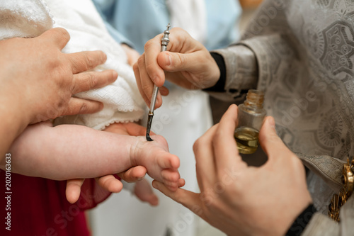 Foto Priest anointing newborn baby foot with holy oil during Orthodox baptism ceremon