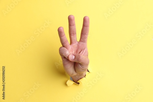 Man showing number three with fingers through hole in yellow paper  closeup