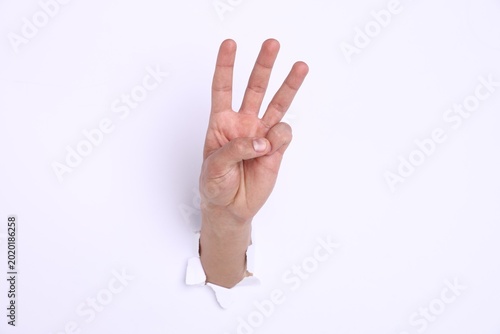Man showing number three with fingers through hole in white paper  closeup
