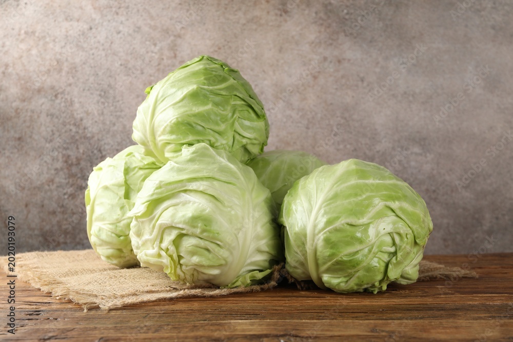 Fototapeta premium Fresh whole cabbages on wooden table against grey background