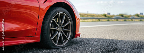 Red car with a flat tire stopped on the side of a highway road. Automobile breakdown service and vehicle maintenance concept. Banner with copy space