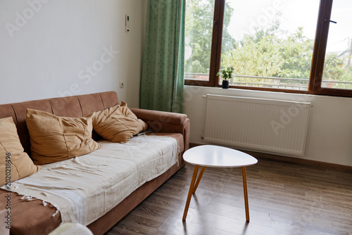 Cozy living room scene with a light brown sofa and a small round table by a bright window, conveying calm, homely comfort and a simple relaxed mood.