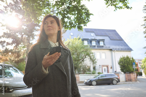 Woman holding smartphone in front of a house with solar panels on the roof