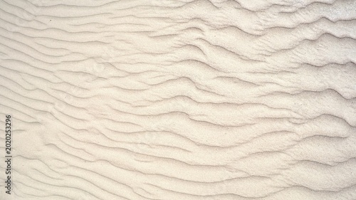 Natural sand texture with wind ripples on a beach. Top view background of wavy desert dunes or coast line for summer vacation concept, abstract organic patterns and minimalist backdrops.