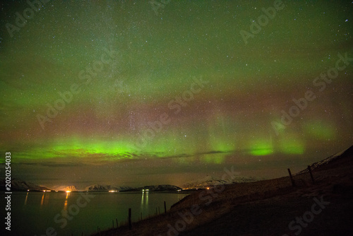 Fotografie Aurora borealis glows over fjord and snowy mountains in North Iceland