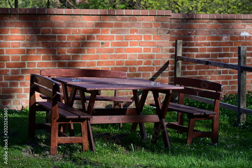 A wooden table and three benches and a brick wall