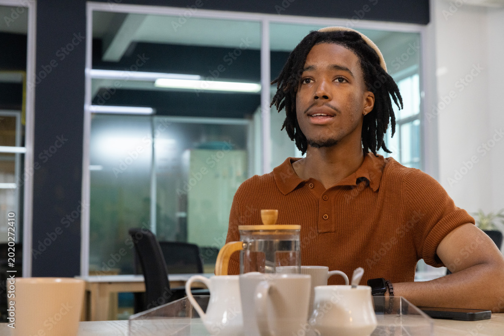 Fototapeta premium African American man sitting at office table in rust polo, French press, copy space