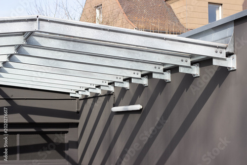 Schilderij op canvas Metal awning structure with galvanized steel beams casting shadows on a dark wal