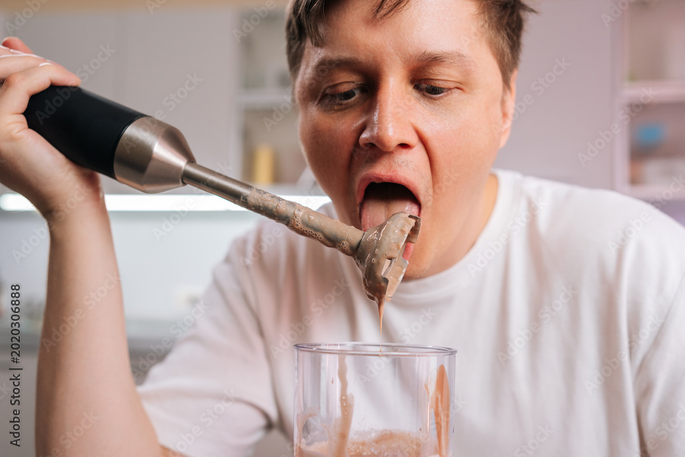 Ταπετσαρία Man tasting smoothie residue from an immersion blender blade with tongue, showing careless and risky behavior while preparing drink in modern kitchen