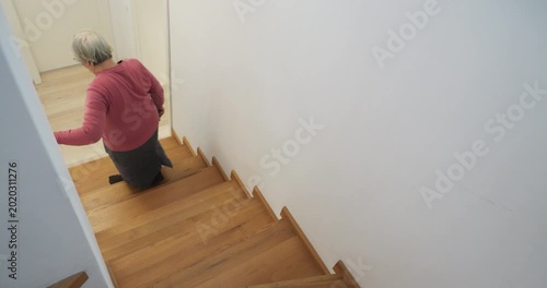 Old woman walking down the wooden stairs of modern house