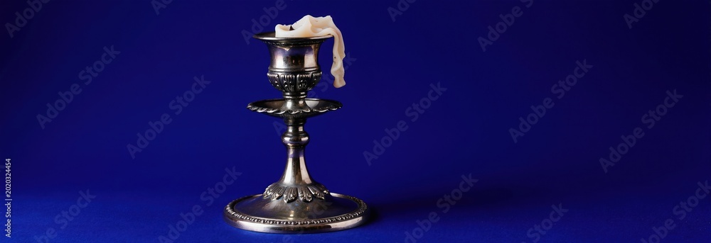 Obraz premium Silver candlestick with melted white candle stands on blue background. Symbolizes waning potency sexual issues old age. Concept loss. Horizontal banner.