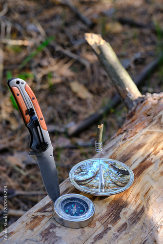 Fotografie Vertical view survival tools, compass, knife, and solar lighter on forest wood