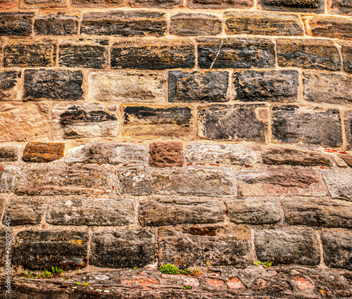 Detailed texture of a curved, ancient stone wall featuring weathered blocks in shades of dark grey, brown, and red from a historic tower or fortress