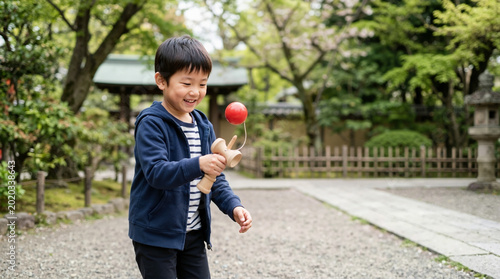 Smiling Japanese boy playing with a traditional wooden kendama toy outdoors. Asian child enjoying a cultural game in a garden setting