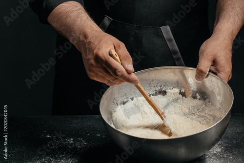 Tableau sur toile Professional baker mixing sourdough dough in metal bowl in dark kitchen for arti