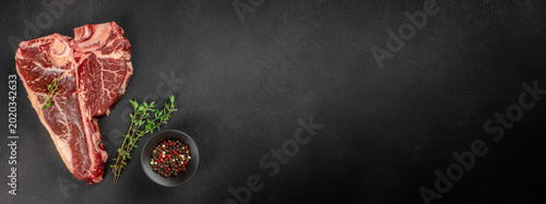 Obraz na plátně Raw tomahawk beef steak with pepper and thyme on black background with copy spac