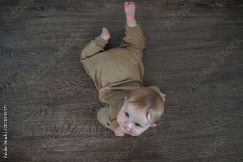 Bild auf Leinwand Top view of an infant lying on a dark wooden floor looking up at the camera