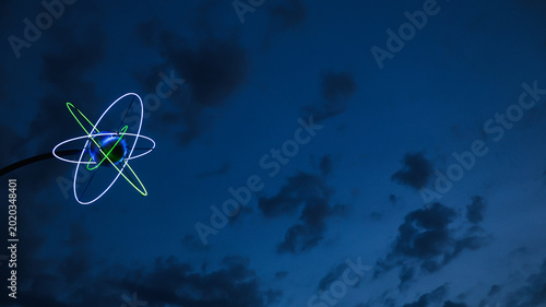Neon light glowing in the evening sky. The shape resembles a retro futuristic sci fi atom that would fit in a space themed concept. The universe and beyond. 