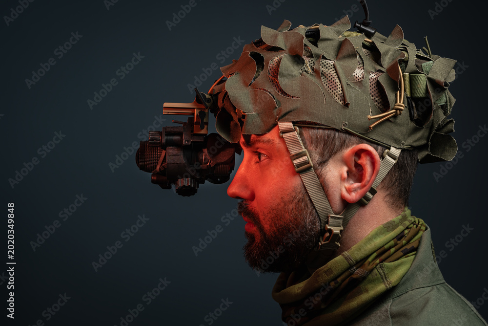 Ταπετσαρία Side view profile of a bearded soldier wearing tactical helmet with night vision device and camouflage scrim on dark background with copy space