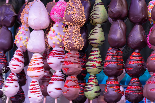 Foto A vibrant display of fresh strawberries dipped in milk, dark, and white chocolate, decorated with nuts and colorful sprinkles at a European food stall