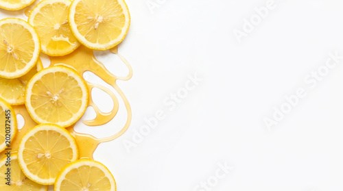 Organic fresh lemon slices with thick golden honey drips and swirls on the far left of a white background with large copy space