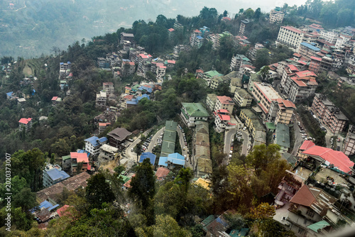 Aerial view of Gangtok city nestled on misty Himalayan hills with dense forests and dramatic cloudy mountain scenery in Sikkim, India.